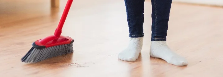 Person fegt mit Besen einen Holzboden